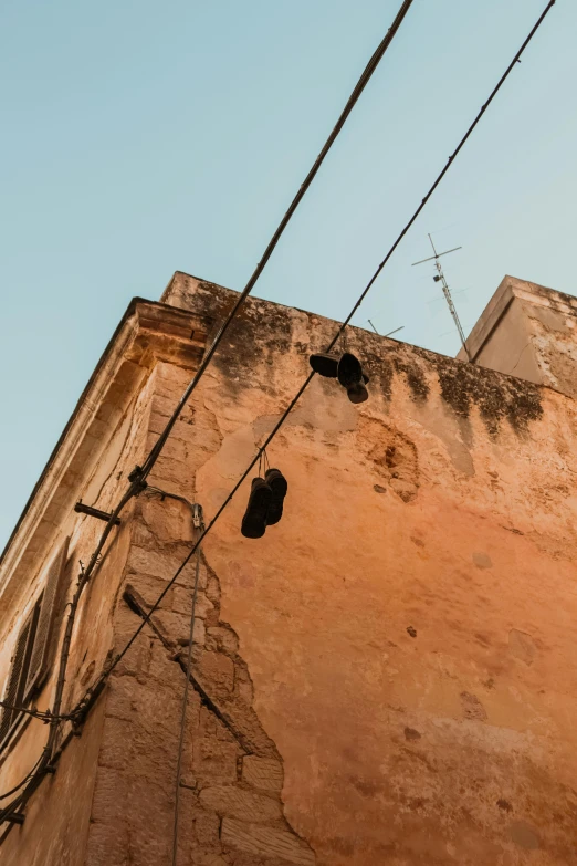 a pair of shoes hanging off the side of a building, trending on pexels, renaissance, old town mardin, cables and wires, warm glow, up there