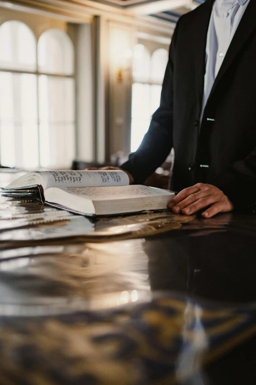 a man in a suit sitting at a table with a book, trending on unsplash, renaissance, in a courtroom, standing inside of a church, glossy surface, thumbnail