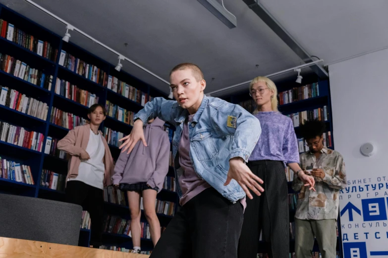 a group of people standing around a man on a skateboard, an album cover, by Emma Andijewska, pexels contest winner, antipodeans, in a library, non binary model, battle pose, greta thunberg