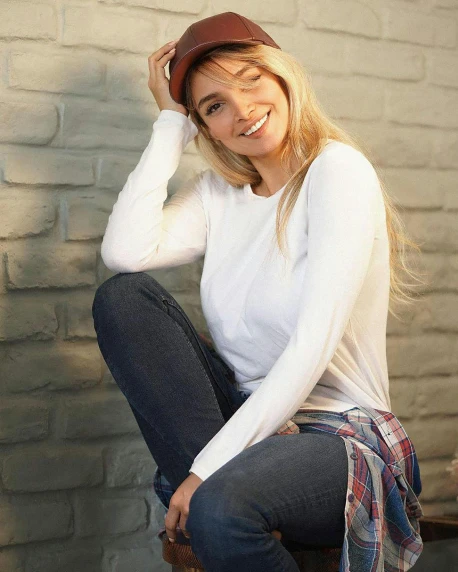 a woman sitting on a bench in front of a brick wall, white baseball hat, evanna lynch, wearing jeans, relaxing and smiling at camera