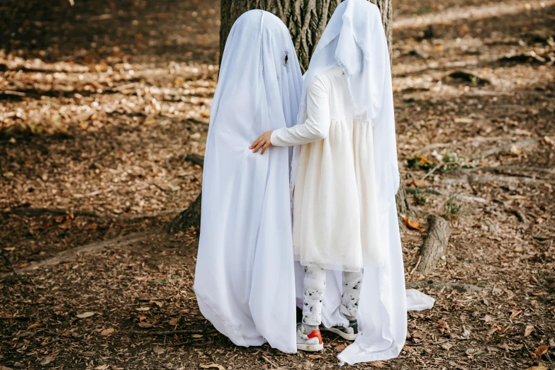 two women dressed in white standing next to a tree, pexels contest winner, surrealism, halloween ghost under a sheet, little boy wearing nun outfit, best friends, headless