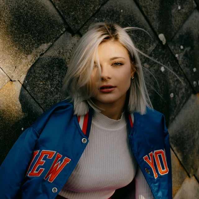 a woman in a new york jacket leaning against a wall, trending on pexels, blue-white hair, portrait sophie mudd, aurora aksnes, low quality photo