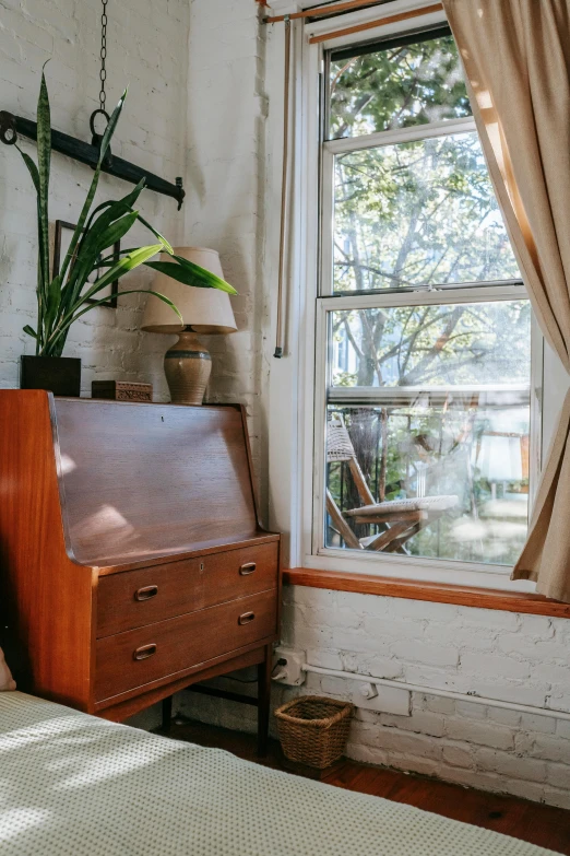 a bed sitting in a bedroom next to a window, unsplash, arts and crafts movement, terrarium lounge area, old furniture, neighborhood outside window, warm colored furniture