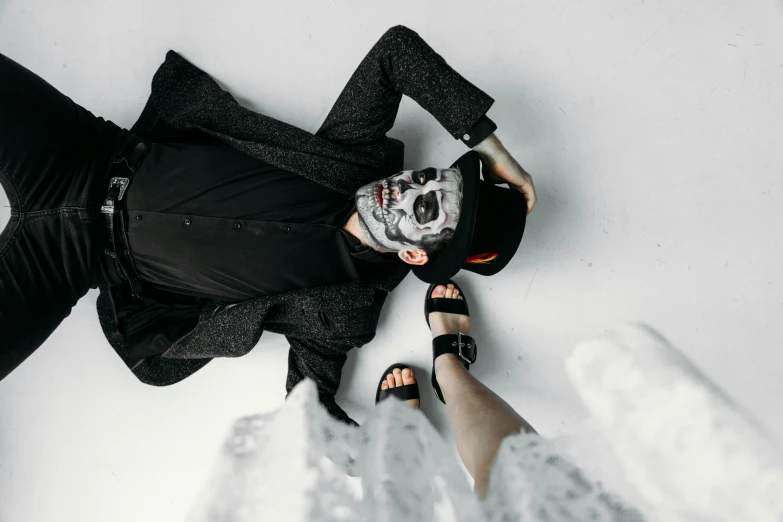 a man laying on top of a white floor next to a woman, by Emma Andijewska, pexels contest winner, lowbrow, skull face paint, full body with costume, black and grey, promotional image