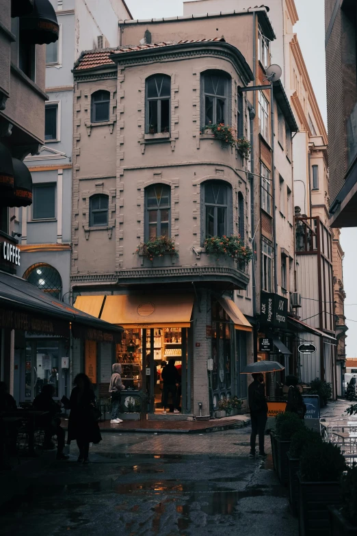 a group of people walking down a street next to tall buildings, by Cafer Bater, pexels contest winner, art nouveau, cozy cafe background, istanbul, beige, rainy evening