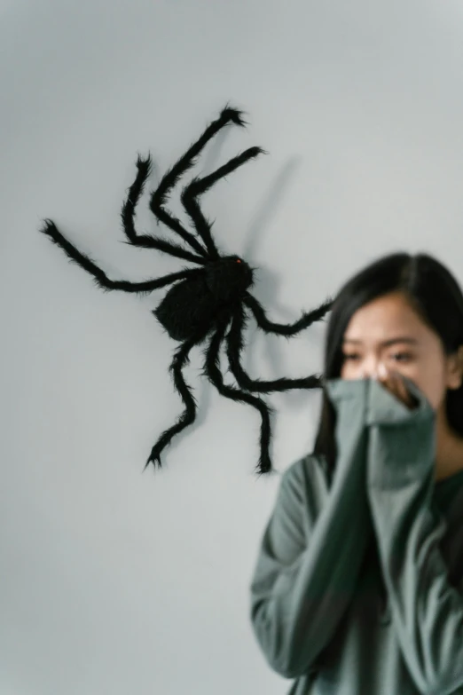 a woman covering her face in front of a fake spider, a cartoon, by Attila Meszlenyi, pexels contest winner, hurufiyya, wenjun lin, beistle halloween decor, profile image, made of lab tissue