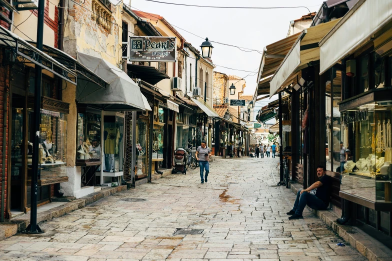 a couple of people that are sitting on a bench, a photo, pexels contest winner, renaissance, lots of shops, cyprus, walking down a street, sparsely populated