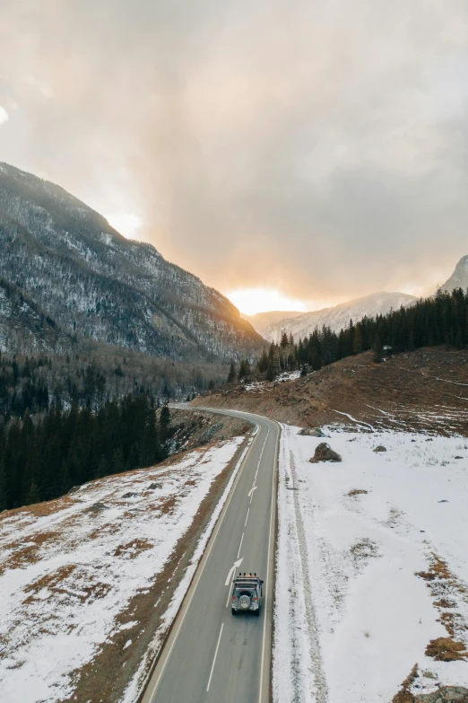 a couple of cars driving down a snow covered road, by Tobias Stimmer, pexels contest winner, minimalism, sunset in a valley, 4 k cinematic panoramic view, rocky mountains, multiple stories