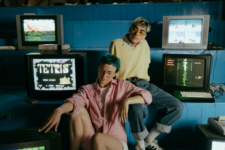 a couple of people that are sitting in front of some televisions, an album cover, pexels, retrofuturism, tetris, federation clothing, arcade cabinet, ivy's