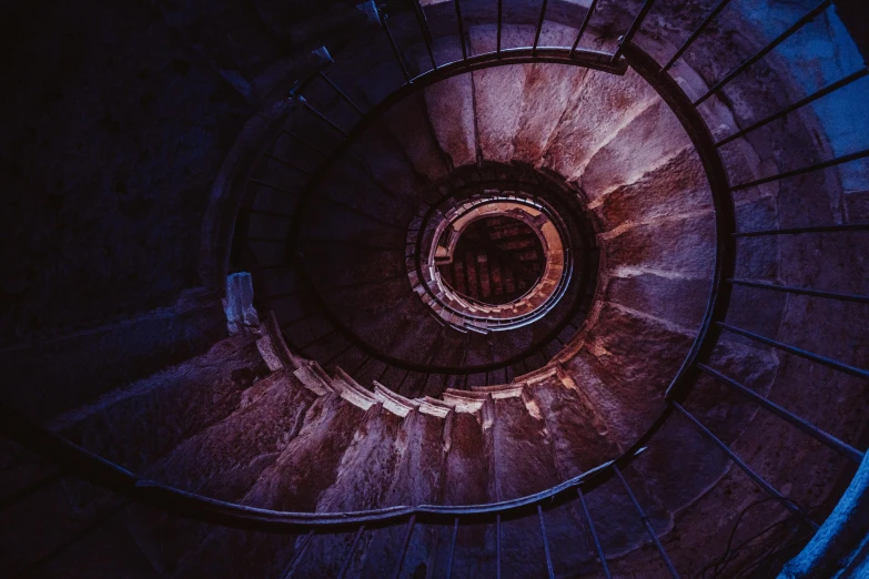 a spiral staircase leading to the top of a building, an album cover, by Adam Marczyński, unsplash contest winner, dark purple lighting, inside a tomb, light red and deep blue mood, camera looking down upon