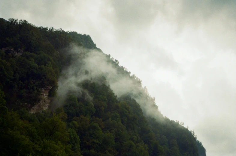 a boat in a body of water with a mountain in the background, smoke - filled ， green hill, looking down a cliff, heavy rain from thick clouds, looking over west virginia