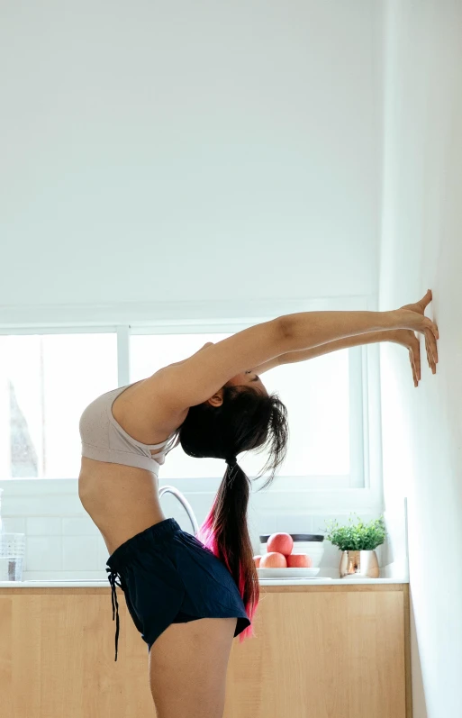 a woman doing a yoga pose in front of a window, pexels contest winner, in a kitchen, waist reaching ponytail, wall corner, head tilted downward