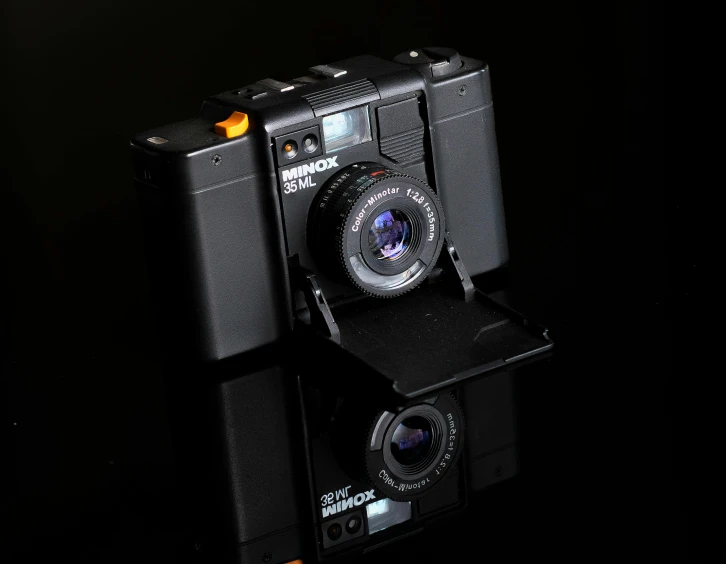 a black camera sitting on top of a table, toy camera, in front of a black background, f/3.2, full body in camera