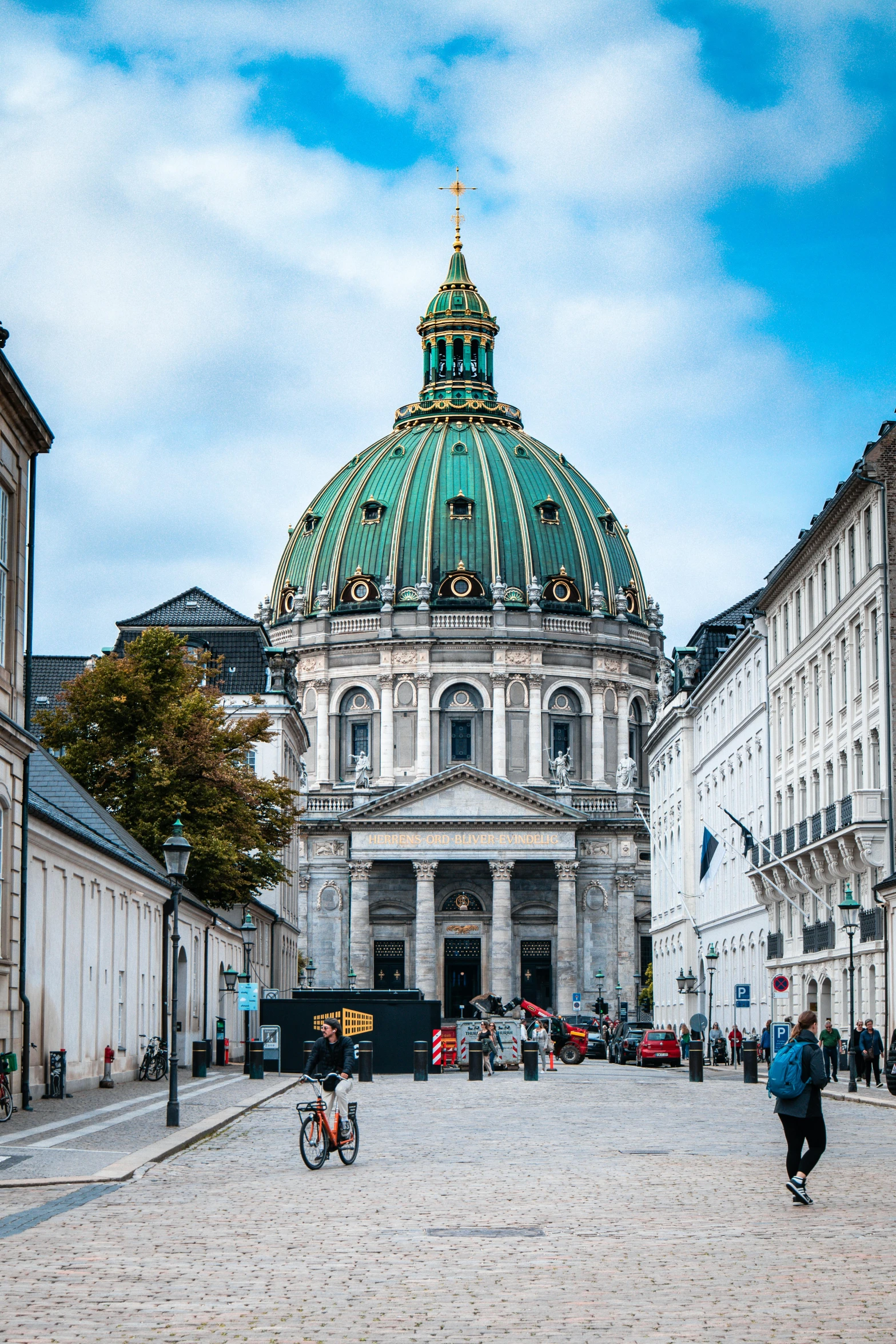 a group of people walking down a cobblestone street, inspired by Heinrich Danioth, pexels contest winner, neoclassicism, neoclassical tower with dome, denmark, exterior view, rounded roof