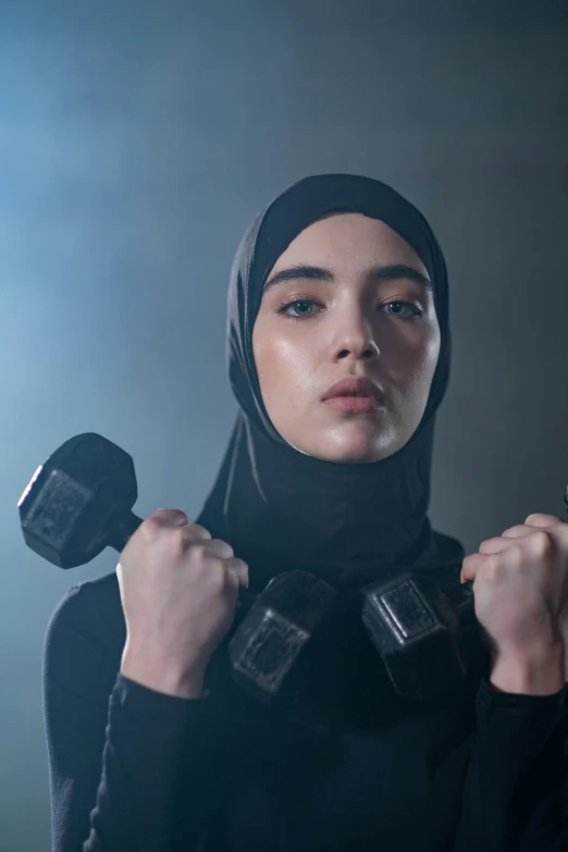 a woman in a hijab is holding a pair of dumbs, an album cover, inspired by Maryam Hashemi, shutterstock, lifting weights, still from the movie ex machina, athletic fashion photography, asian human