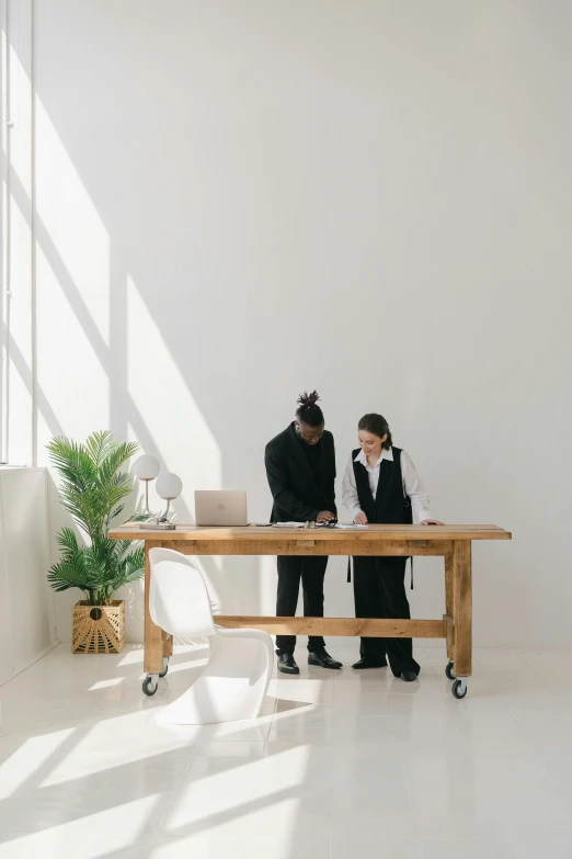 a couple of men standing next to each other in a room, trending on unsplash, visual art, white table, wooden table, ecommerce photograph, designer furniture