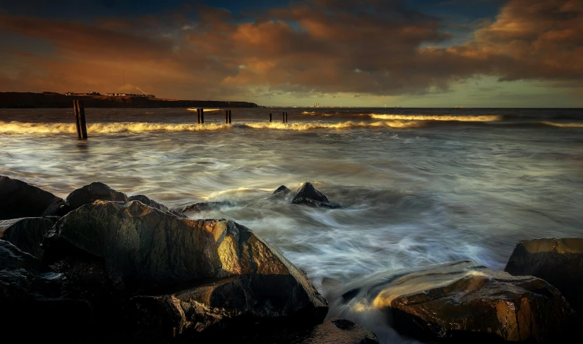 a group of rocks sitting on top of a beach next to the ocean, by Peter Churcher, pexels contest winner, romanticism, towering waves, maryport, moody evening light, rivulets