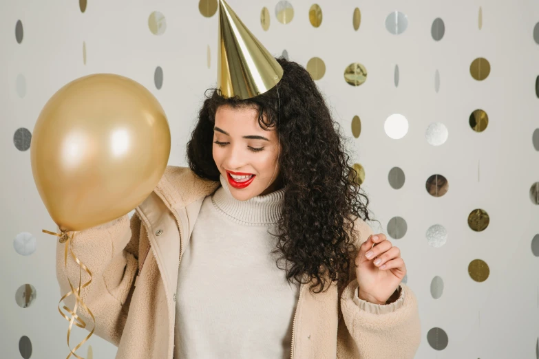 a woman in a party hat holding a balloon, trending on pexels, gold clothes, brown curly hair, wearing a grey hooded sweatshirt, bubbly