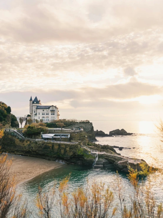 a white house sitting on top of a hill next to a body of water, inspired by Juan de Flandes, pexels contest winner, renaissance, beaches, golden hour 4k, gunma prefecture, located in a castle