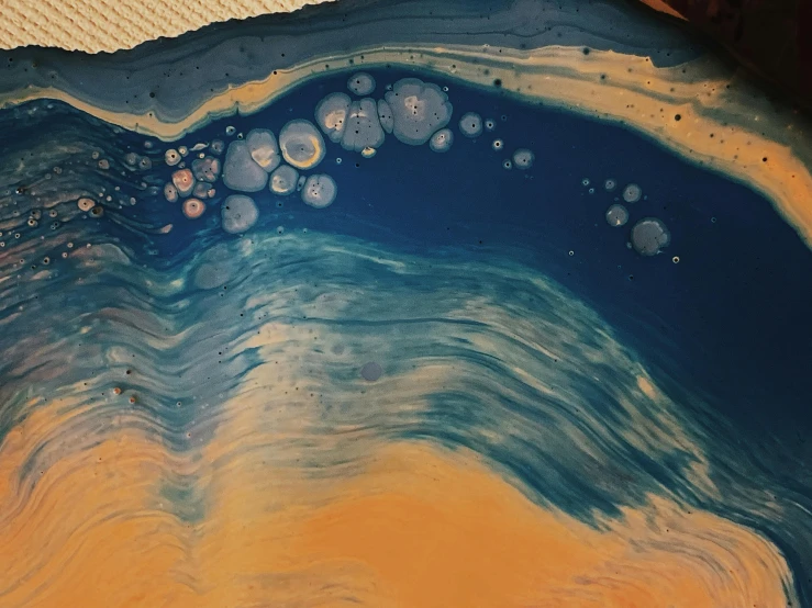 a close up of a piece of art on a table, inspired by Katsuchika Hokusai, trending on unsplash, process art, bubbly, blue and orange tones, detailed painting of dune movie, oil spill