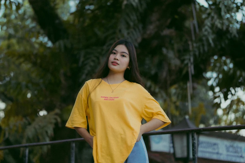 a woman standing in front of a fence wearing a yellow shirt, pexels contest winner, in tshirt, asian girl, ad image, oversized