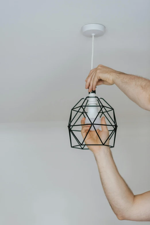 a man holding a light fixture in his hand, pexels contest winner, geometric style, with a white background, simple structure, hanging