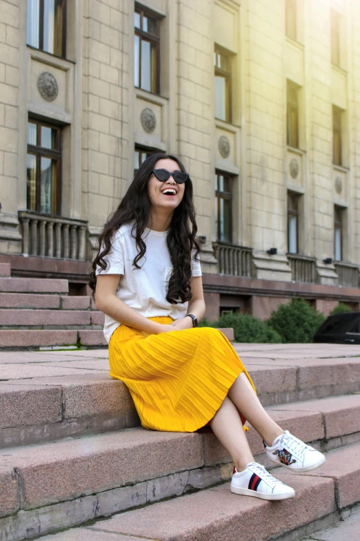 a woman sitting on the steps of a building, wearing a modern yellow tshirt, pleated skirt, in russia, bright and happy