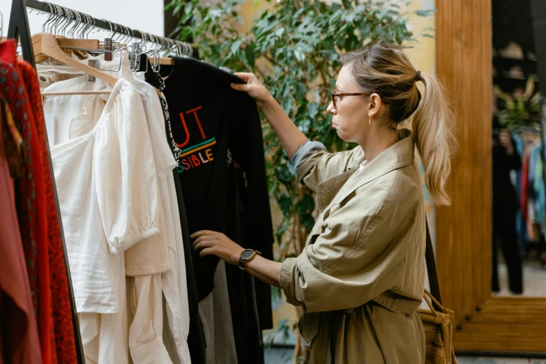 a woman standing in front of a rack of clothes, trending on pexels, renaissance, inspect in inventory image, wearing a light shirt, foliage clothing, fast paced