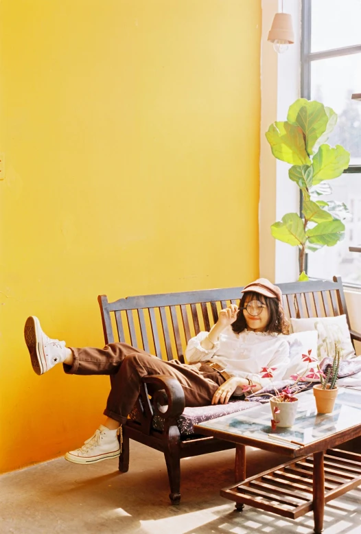 a person laying on a couch in front of a window, an album cover, inspired by Wes Anderson, large potted plant, hong june hyung, yellow walls, enjoying coffee at a coffee shop