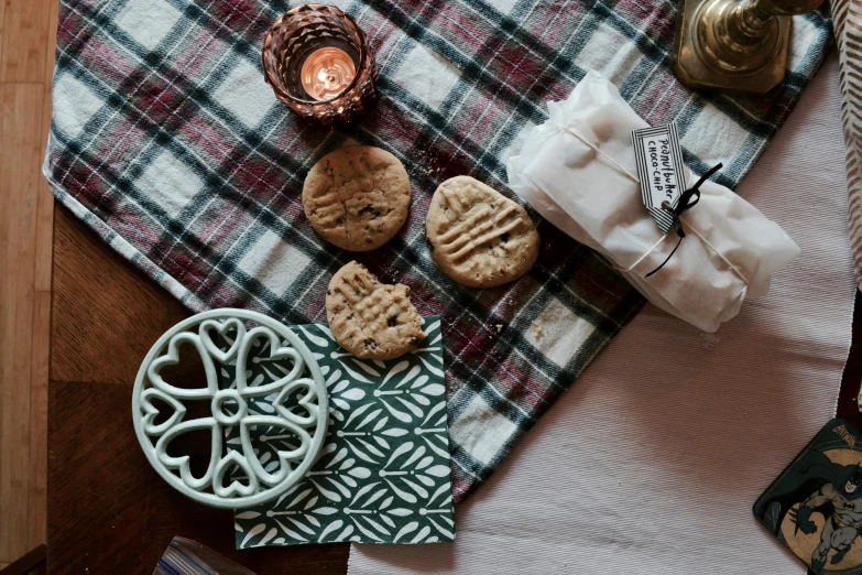 a table topped with a plate of cookies next to a candle, inspired by Richmond Barthé, unsplash, private press, tartan scarf, holding mesh bag with bagels, studio product shot, tablecloth