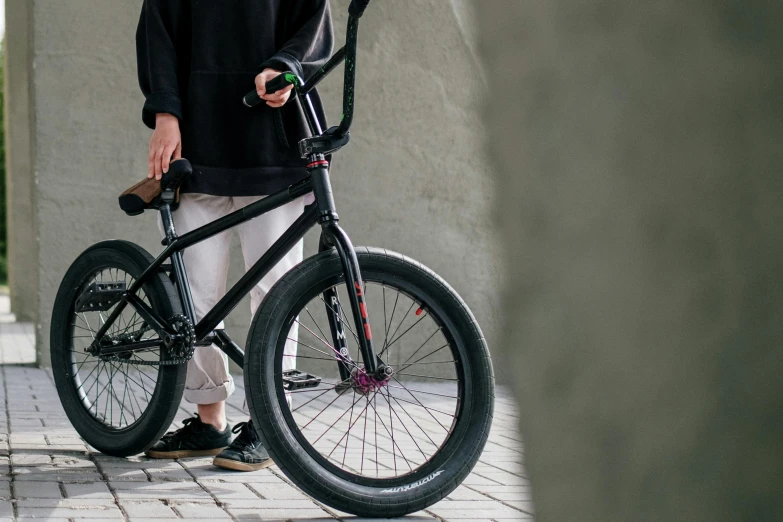 a man standing next to a bicycle on a sidewalk, inspired by Seb McKinnon, unsplash, at a skate park, black rims, detailed product shot, bulky build