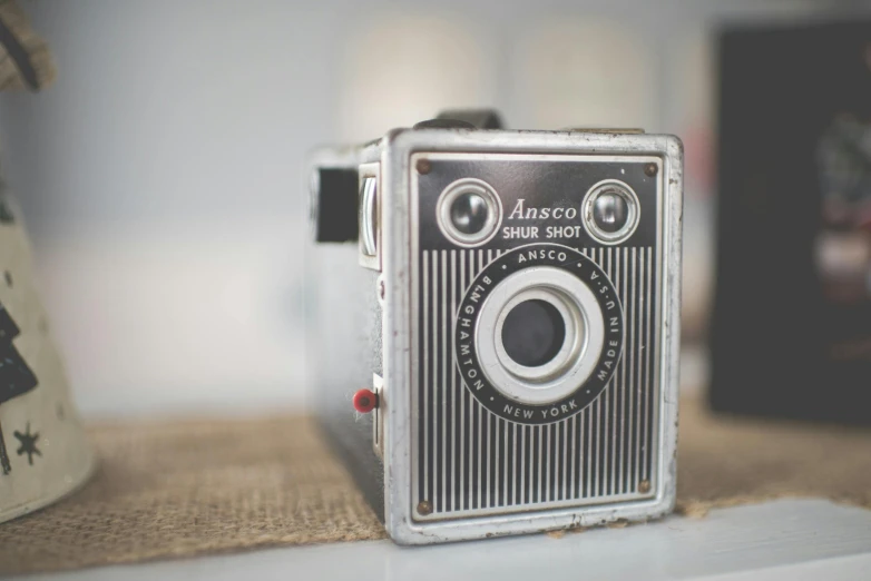 an old camera sitting on top of a table, style of pinhole photography, lovingly looking at camera, grey metal body, ansel ]