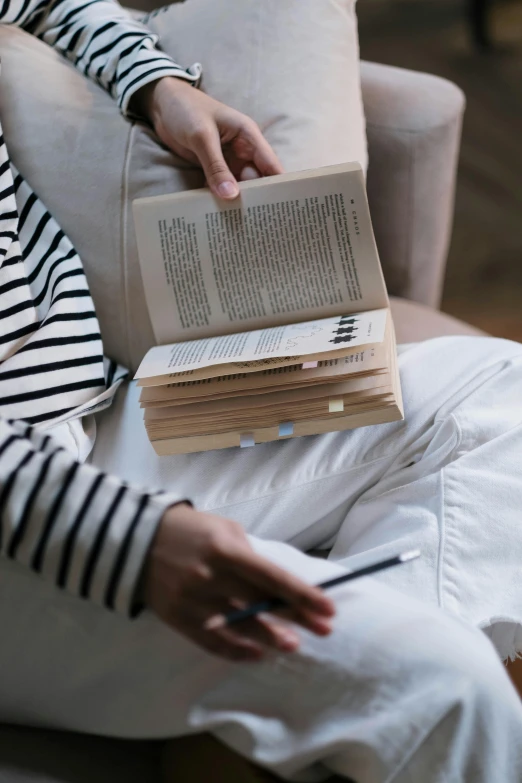 a woman sitting on a couch reading a book, pexels contest winner, holding a stack of books, streamlined spines, annotations, full body close-up shot