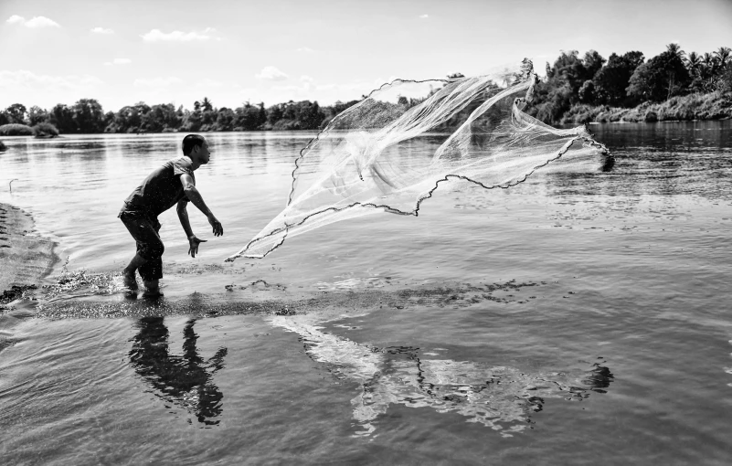 a man that is standing in the water with a net, a black and white photo, net art, nile river environment, thawan duchanee, two hands reaching for a fish, on a riverbank