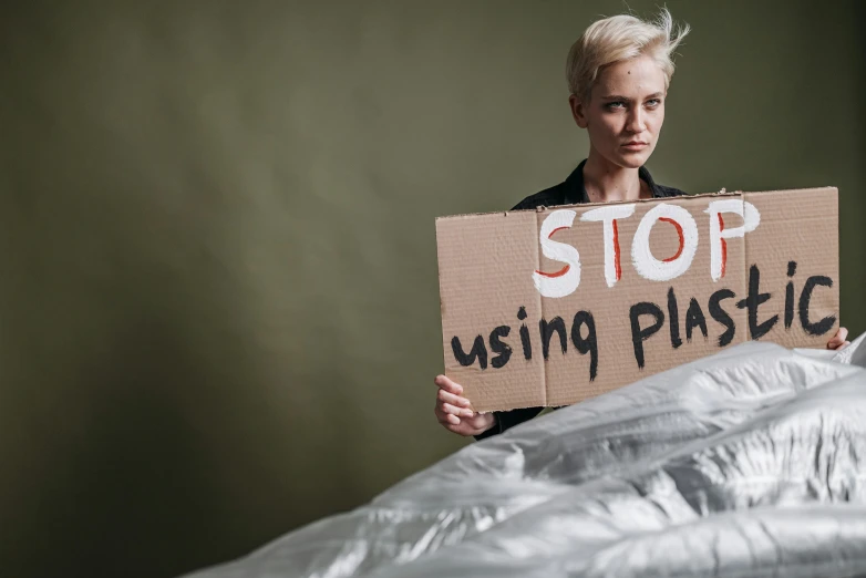 a woman holding a sign that says stop using plastic, unsplash, plasticien, un made bed, avatar image, sculpting, johan liebert