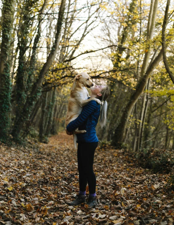 a woman holding a dog in her arms in the woods, by Arabella Rankin, pexels contest winner, blond, november, woodland location, profile image