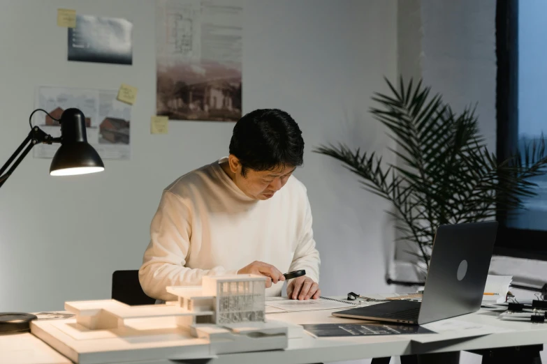 a woman sitting at a desk working on a laptop, a drawing, by Jang Seung-eop, pexels contest winner, light and space, asian man, architect studio, slight overcast lighting, lachlan bailey