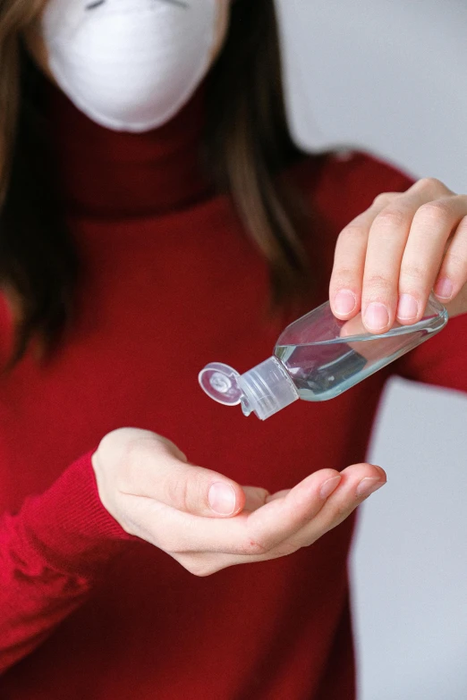 a woman wearing a face mask holding a bottle of hand sanitizer, a picture, shutterstock, renaissance, on grey background, square, holiday, made of plastic