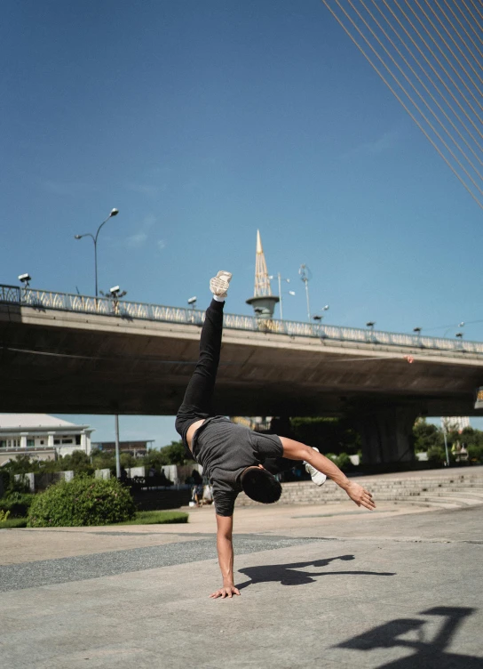 a man doing a handstand in front of a bridge, a picture, street photo, profile image, bangkok, high quality image