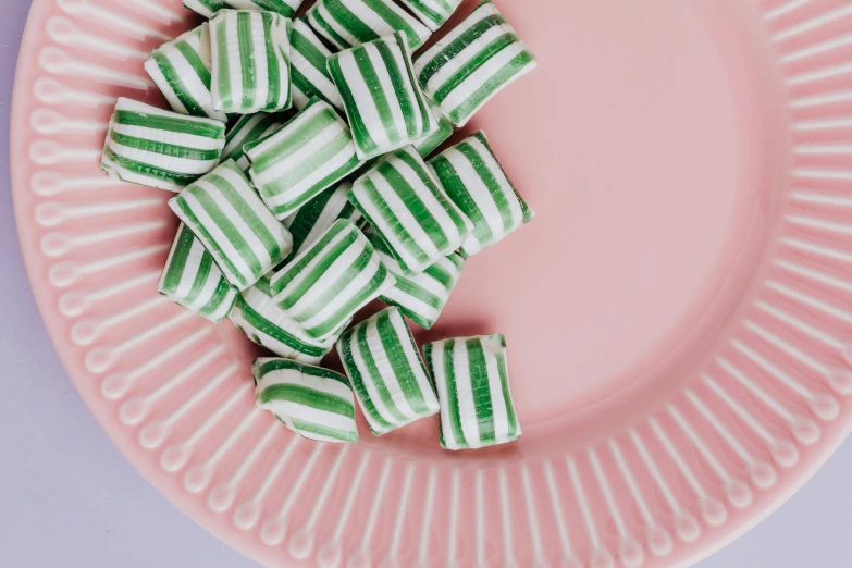 a pink plate topped with green and white candy, by Emma Andijewska, trending on pexels, striped, bandoliers, sydney hanson, green: 0.5