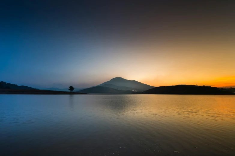 a large body of water with a mountain in the background, by Saurabh Jethani, unsplash contest winner, minimalism, crepuscule, willow tree and hill, multicoloured, light and dark