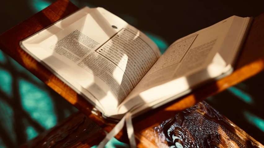 an open book sitting on top of a wooden table, unsplash, hurufiyya, sparkling in the sunlight, brown, religious iconography, thumbnail