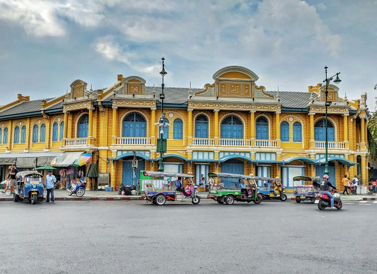 a group of motorcycles parked in front of a yellow building, thai architecture, trams, an victorian city, indigo