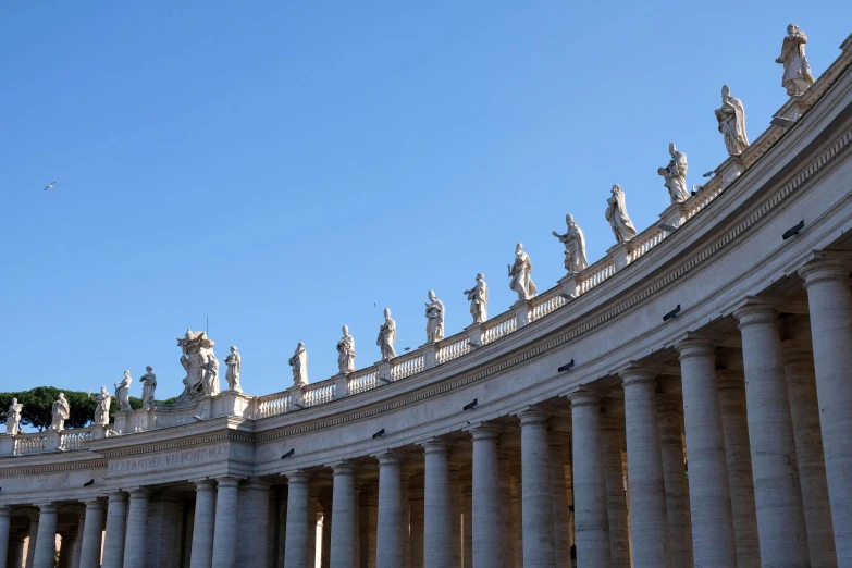 a group of statues that are on the side of a building, by Cagnaccio di San Pietro, pexels contest winner, neoclassicism, clear blue skies, colonnade, john paul ii, shot from afar