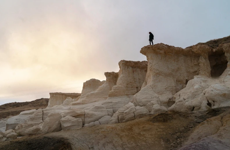 a person standing on top of a rock formation, white clay, epic land formations, carson ellis, gigapixel photo