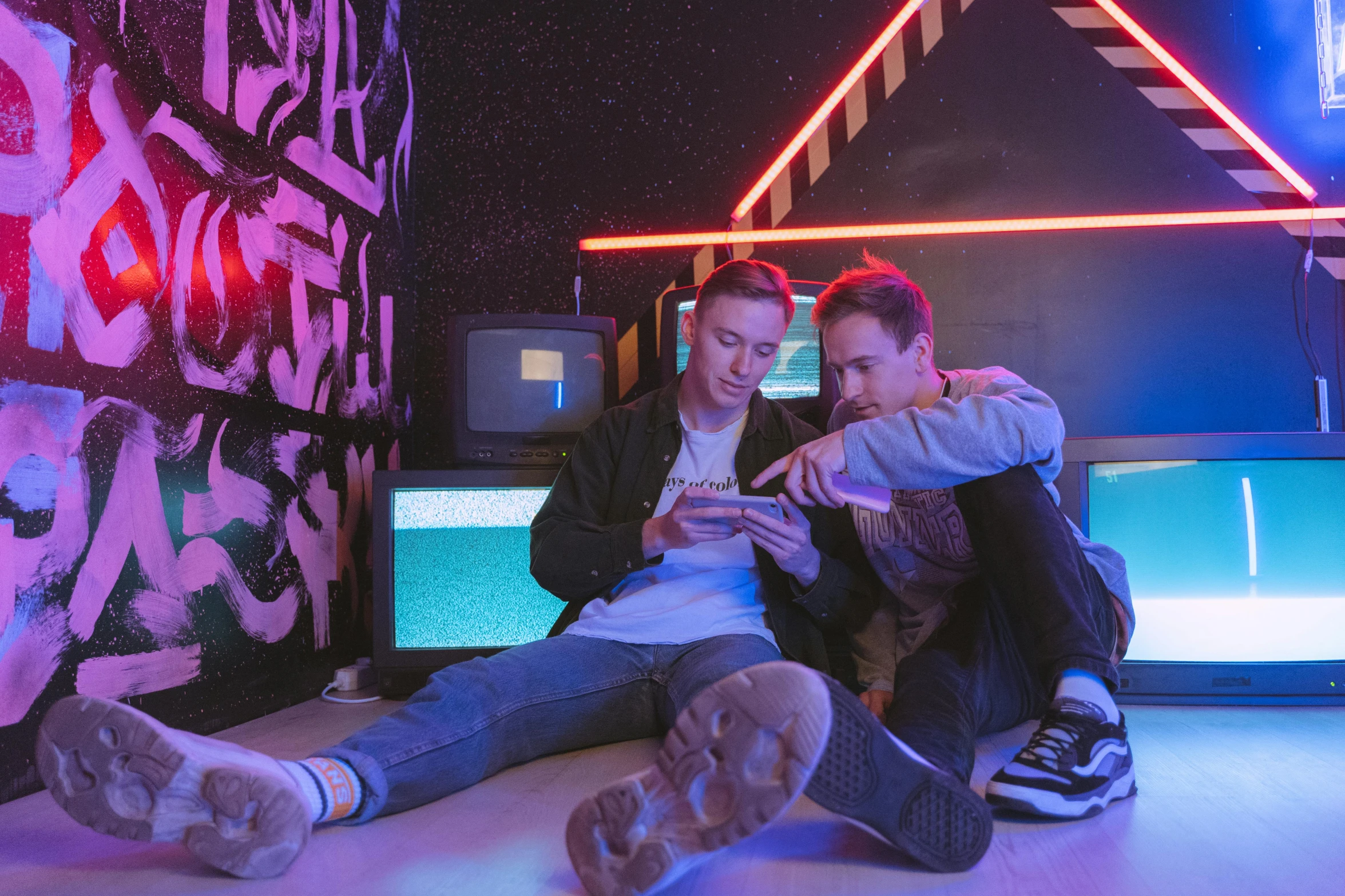 a couple of men sitting next to each other on a floor, pexels contest winner, interactive art, in a cyberpunk themed room, teenage boy, vhs style, selfie