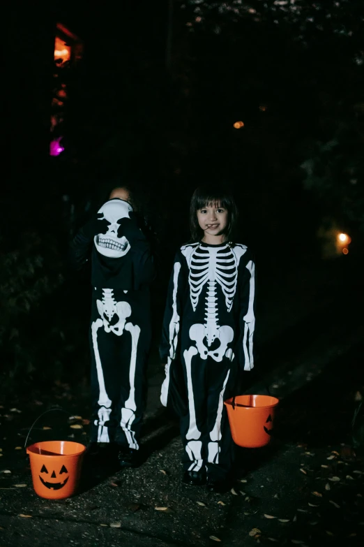 a couple of kids standing next to each other in halloween costumes, by Helen Stevenson, pexels, process art, glowing bones, kodak film, human skulls on ground, snacks