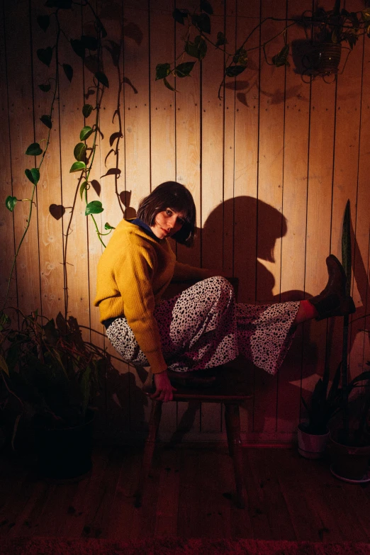 a woman sitting on a chair in a dark room, an album cover, inspired by Elsa Bleda, trending on pexels, yellow clothes, long shadow, covered in plants, taken in the late 1980s