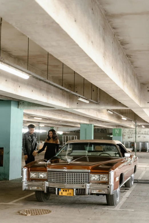 a group of people standing around a car in a parking garage, inspired by Elsa Bleda, brutalism, swagger! lowrider culture, promo image, couple, 3 / 4 wide shot