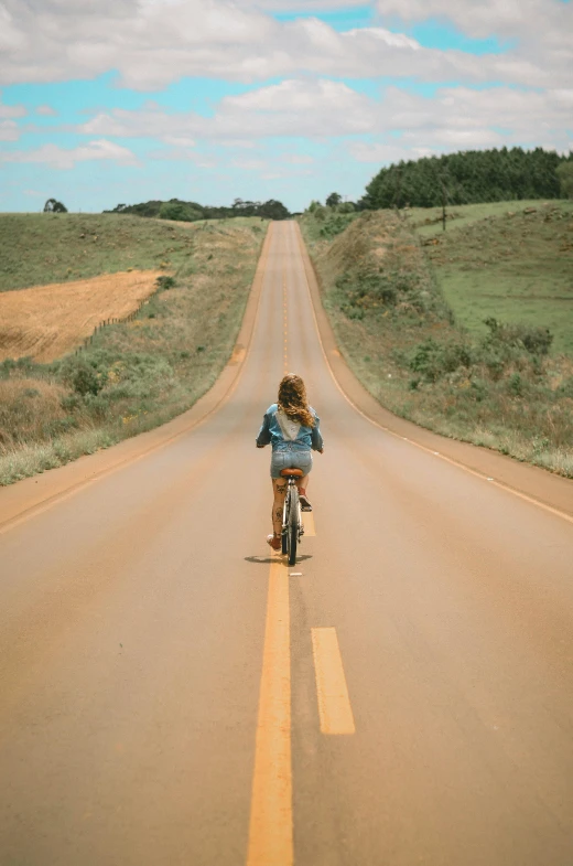 a woman riding a bike down the middle of a road, australia, brazilian, 🚿🗝📝, in the countryside